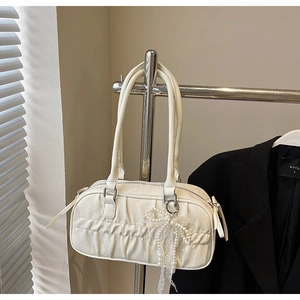 Detailed view of white pleated handbag featuring a pearl and lace bow charm on metal hanger