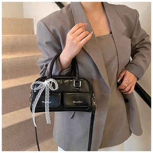 Detail of glossy black PU leather bag with white lace bow and front flap pockets