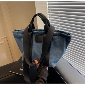 Détail du sac cabas en denim bleu avec patch logo en cuir et bandoulière en nylon noir chic