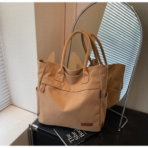 Close-up of khaki canvas tote bag featuring brown leather KHBAG logo and side pockets