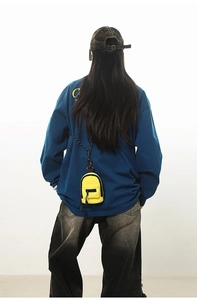 Detail of a bright yellow mini backpack pendant with black lanyard on a navy sweatshirt