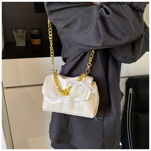 Detail of cream square bag with gold chain, lace bow and pearl charm decorations