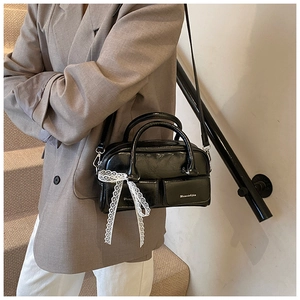 Detail of black glossy leather handbag featuring white lace bow and adjustable strap