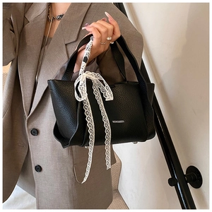 Close-up of black lychee grain leather bucket bag with white lace bow decoration