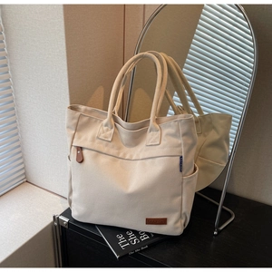 Detail of cream canvas tote bag showing side pocket, leather logo and durable handle