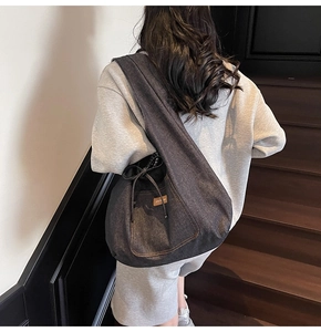 Detail of denim tote bag showing drawstring side and leather patch during model carry
