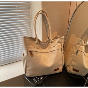 Detail of beige canvas tote bag with leather logo tag and side pocket in soft natural light