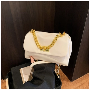 Detailed view of white crossbody bag with thick gold chain handle on wood background