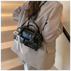 Detail of black glossy handbag with white lace bow and multi-pocket design on stairs