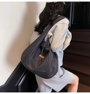 Detail of blue denim tote bag with drawstring bow and brown leather logo tag on the side