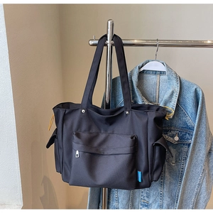 Detail of a black large-capacity tote bag with yellow drawstring side pockets and front zip