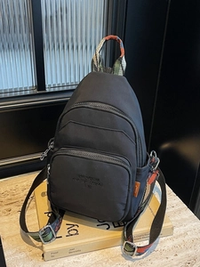 Versatile black nylon chest bag with colorful geometric strap shown on a stack of books