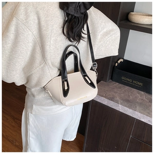Detail view of beige leather bucket bag with black top handles and white contrast stitching