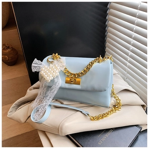 Detail of light blue crossbody bag with gold chain and lace bow charm on beige clothing