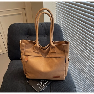 Detail view of large canvas tote bag showing side pocket and brown leather logo patch