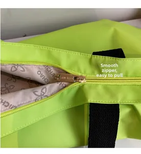 Detail of smooth gold metal zipper and branded interior lining on fluorescent green tote