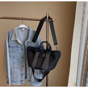 Détail du sac cabas en toile noire avec bandoulière large amovible et étiquette en cuir