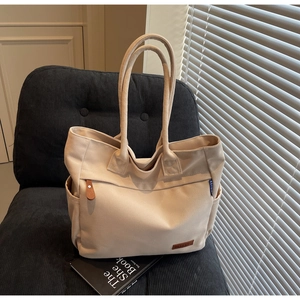 Close-up of cream canvas tote bag with brown leather accents on a grey corduroy chair