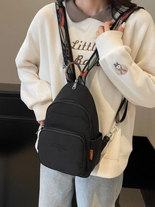 Black nylon mini backpack with colorful jacquard strap worn as a crossbody chest bag