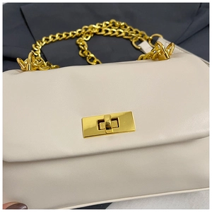 Close-up of cream square bag with gold twist lock and chunky chain strap on grey fabric
