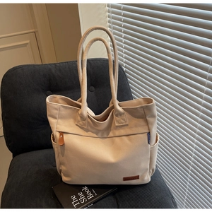 Detailed side view of beige canvas tote bag with side pocket and leather logo patch