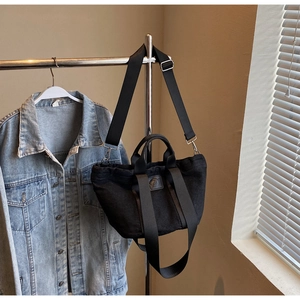 Détail du sac cabas en denim noir avec écusson logo, anses solides et bandoulière réglable