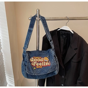 Close-up of vintage denim messenger bag featuring vibrant star embroidery and slogan