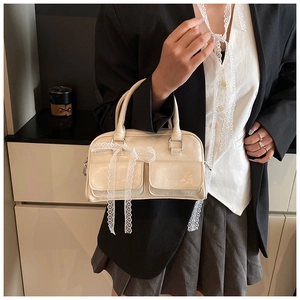 Detail of cream crossbody bag with front flap pockets and white lace ribbon bows