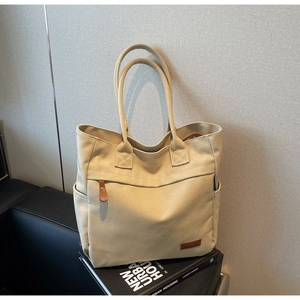 Detailed close-up of a beige canvas tote bag with front pocket and leather logo tag
