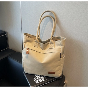 Close-up of beige canvas tote bag detailing reinforced handles and leather zipper pull