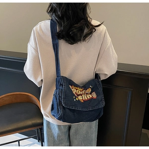 Detail of dark blue denim crossbody bag featuring colorful embroidery and star motifs