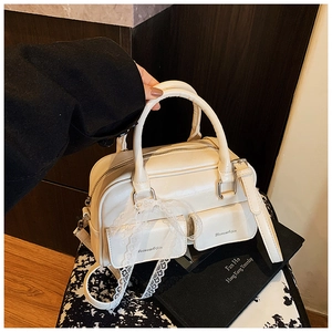 Detail of cream white Boston bag with lace ribbon and brand pocket on dark wood