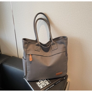Detail of grey canvas tote bag featuring brown leather zipper pull and side pockets