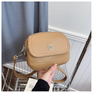 Detailed close-up of light brown crossbody bag with double zippers and metal MB logo