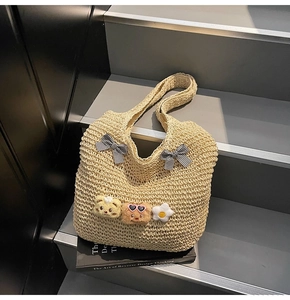 Gros plan d'un sac cabas tissé beige avec des nœuds vichy noirs et des breloques en peluche