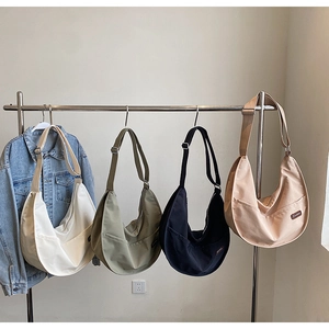 Detailed view of half-moon canvas crossbody bags in four colors hanging on a rack