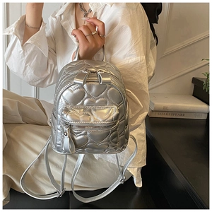 Close-up of silver quilted heart pattern backpack with metallic finish held by model