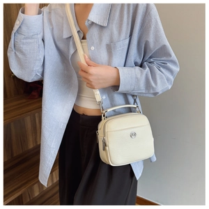Dettaglio di una borsa a tracolla beige crema con trama martellata e logo in metallo