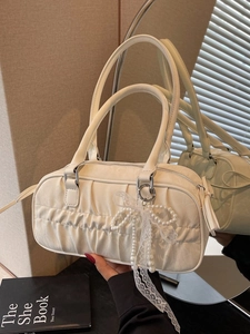 White pleated bowling bag with pearl bow charm and dual handles in a soft studio setting
