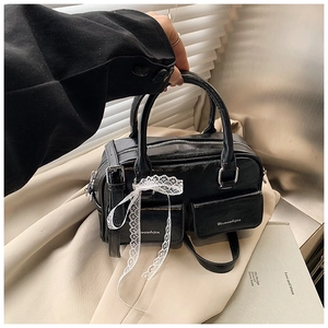 Detail of black pleated Boston bag with twin pockets and a delicate white lace bow