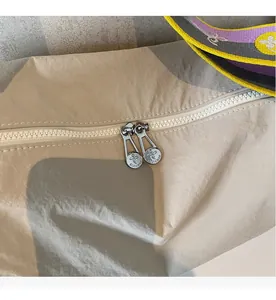 Detail of silver dual zippers with floral engraving and colorful woven strap on beige bag