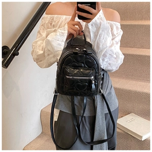 Close-up of heart-quilted black mini backpack worn by model in a casual urban setting