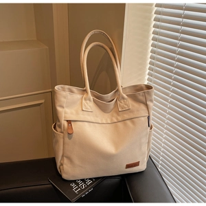 Detail of beige canvas tote bag showing side pocket and leather logo on a leather chair