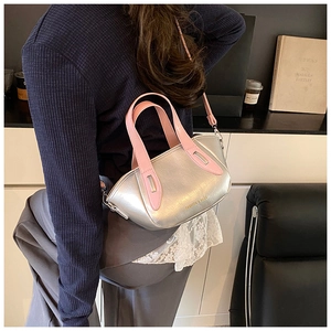 Detail of silver metallic crossbody bucket bag with pink handles worn by a model