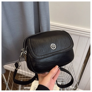 Close-up of black textured crossbody bag featuring silver circular logo and dual metal zippers