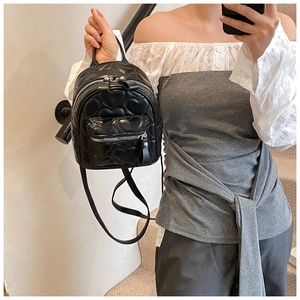 Mirror selfie showing a black quilted mini backpack with heart-shaped stitching detail