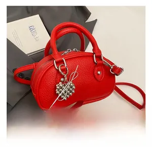 Détail du sac polochon en cuir rouge grainé avec breloque cœur et bandoulière