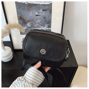 Detail of minimalist black leather crossbody bag with silver hardware and double zippers