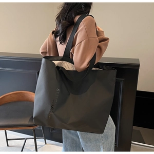 Detail of black large capacity tote bag with logo on shoulder of model in casual setting
