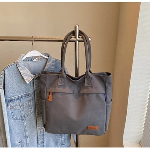 Detail of grey canvas tote bag featuring brown leather logo and spacious side pocket